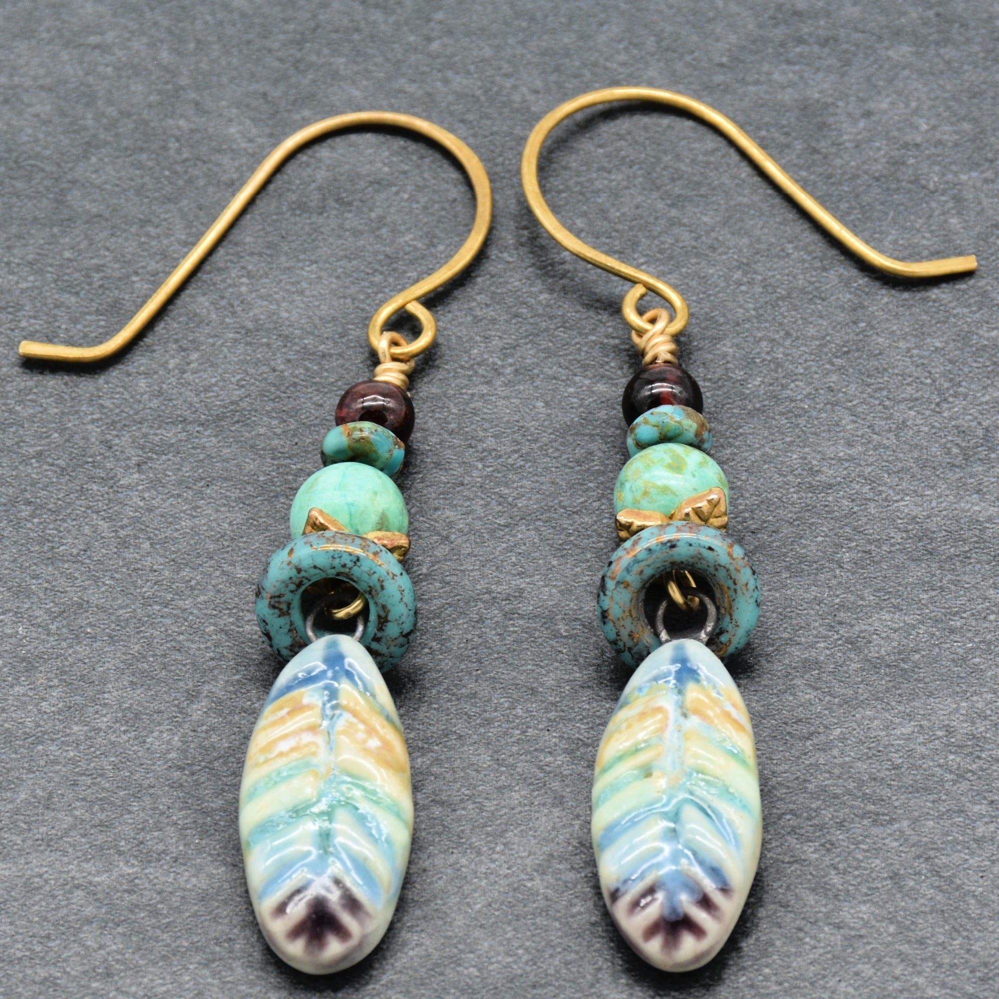 Pair of earrings with turquoise beads and colorful ceramic elements on a gray background