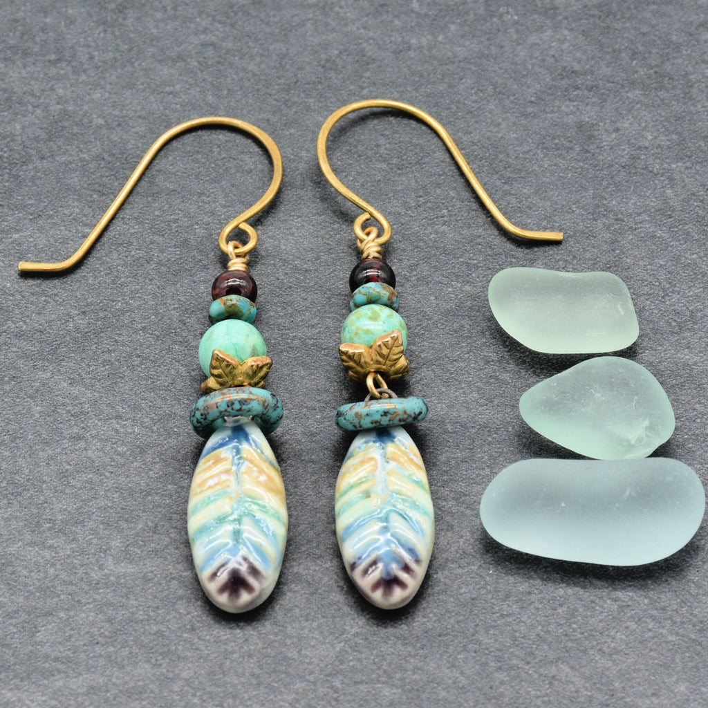 Pair of earrings with decorative beads on a gray surface with three pieces of sea glass.