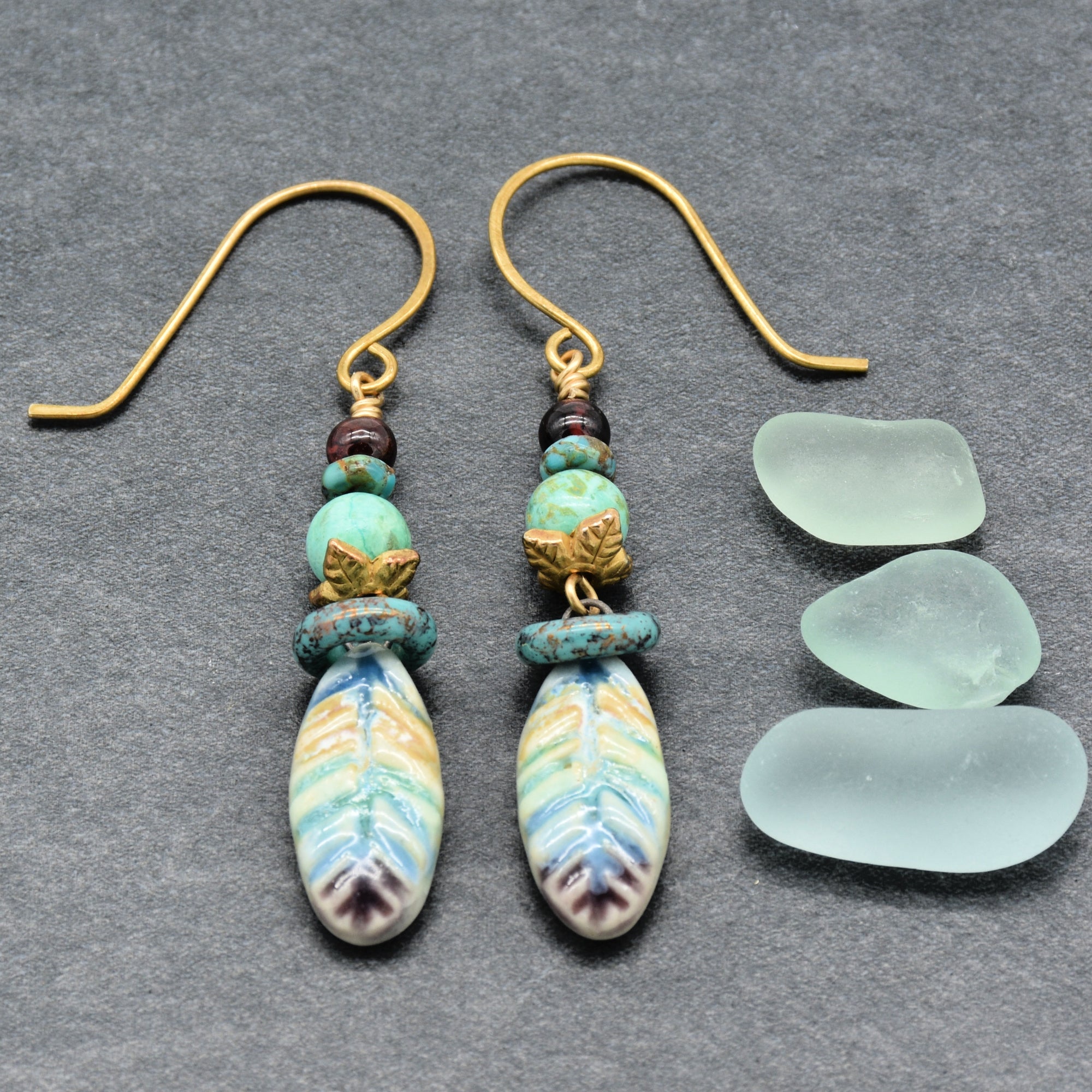 Pair of earrings with decorative beads on a gray surface with three pieces of sea glass.