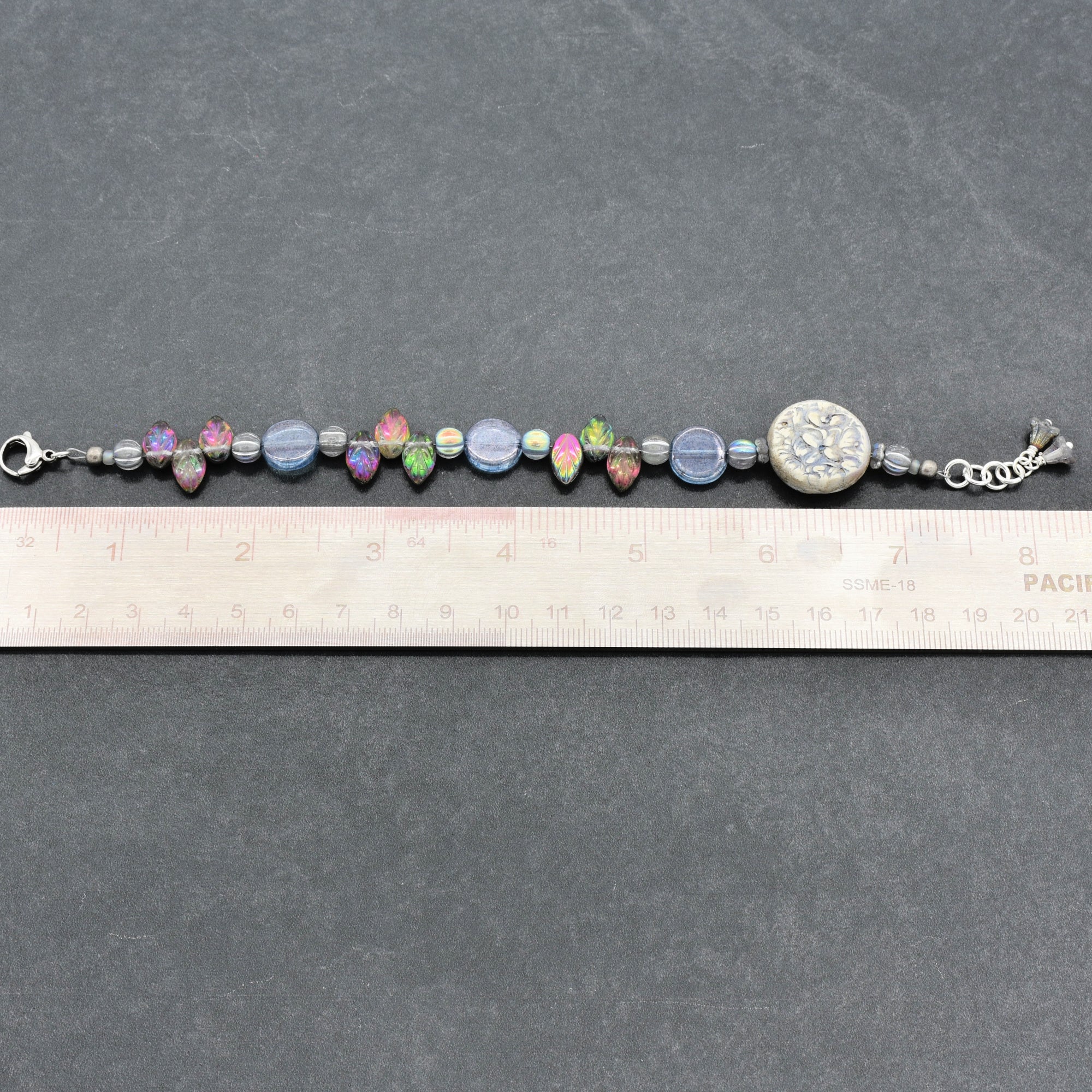 Beaded bracelet on a ruler for size reference against a gray background