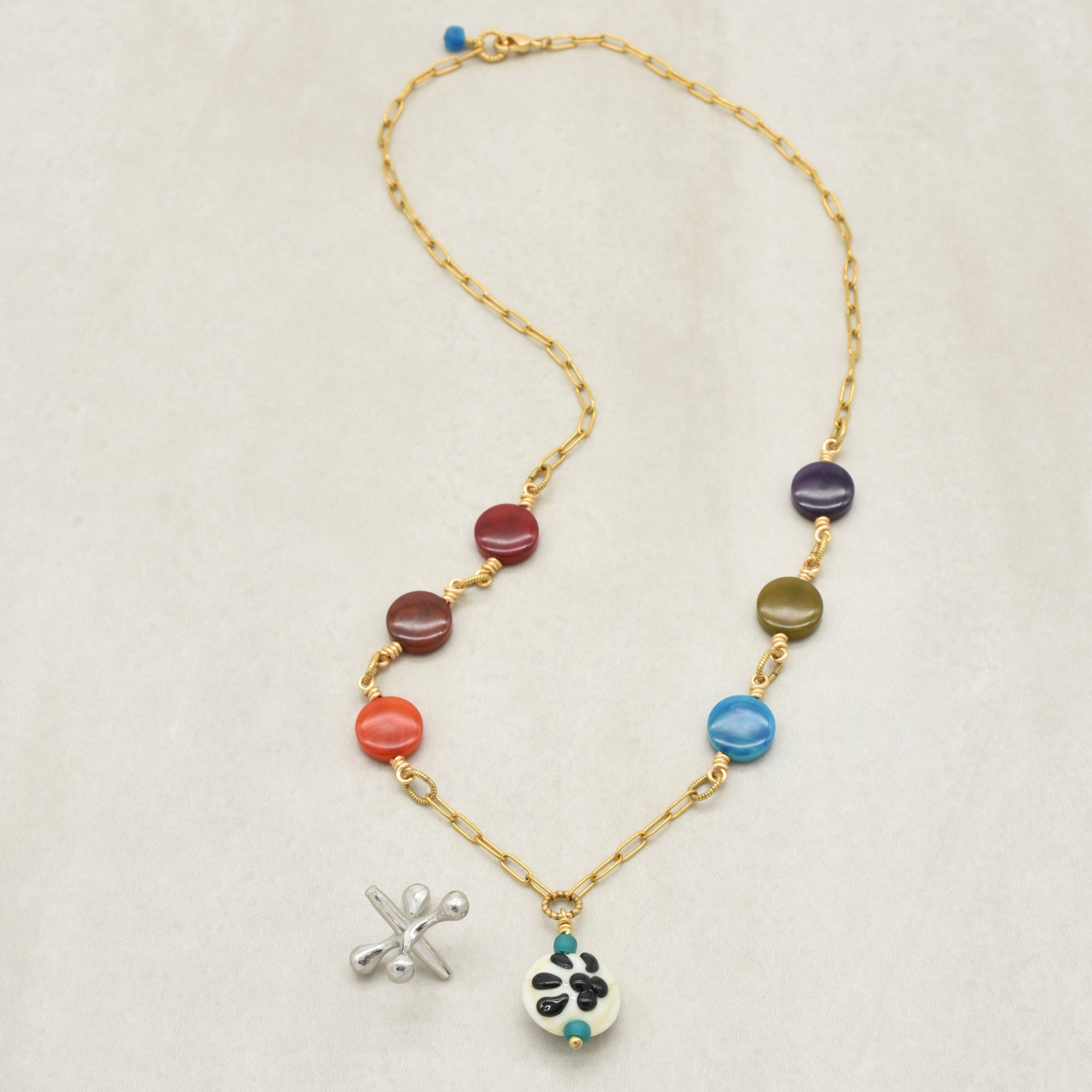 A gold chain necklace featuring colorful round beads in red, orange, blue, green, and purple, with a white paw print charm with black paw pads - made with love in Colorado by Ruby Acorn.