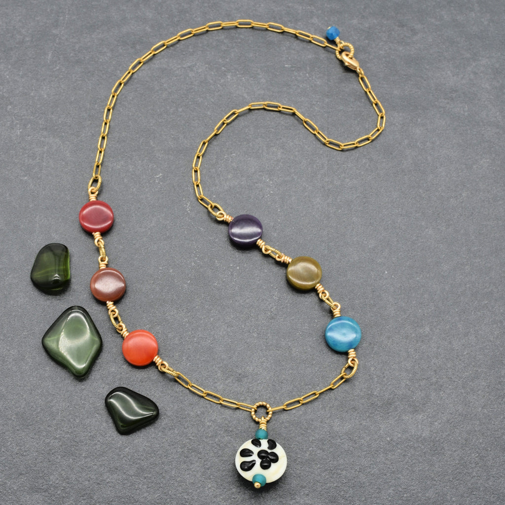 A gold chain necklace with colorful tagua nut coin beads and a white paw print pendant, displayed on a textured gray background - made with love in Colorado by Ruby Acorn.