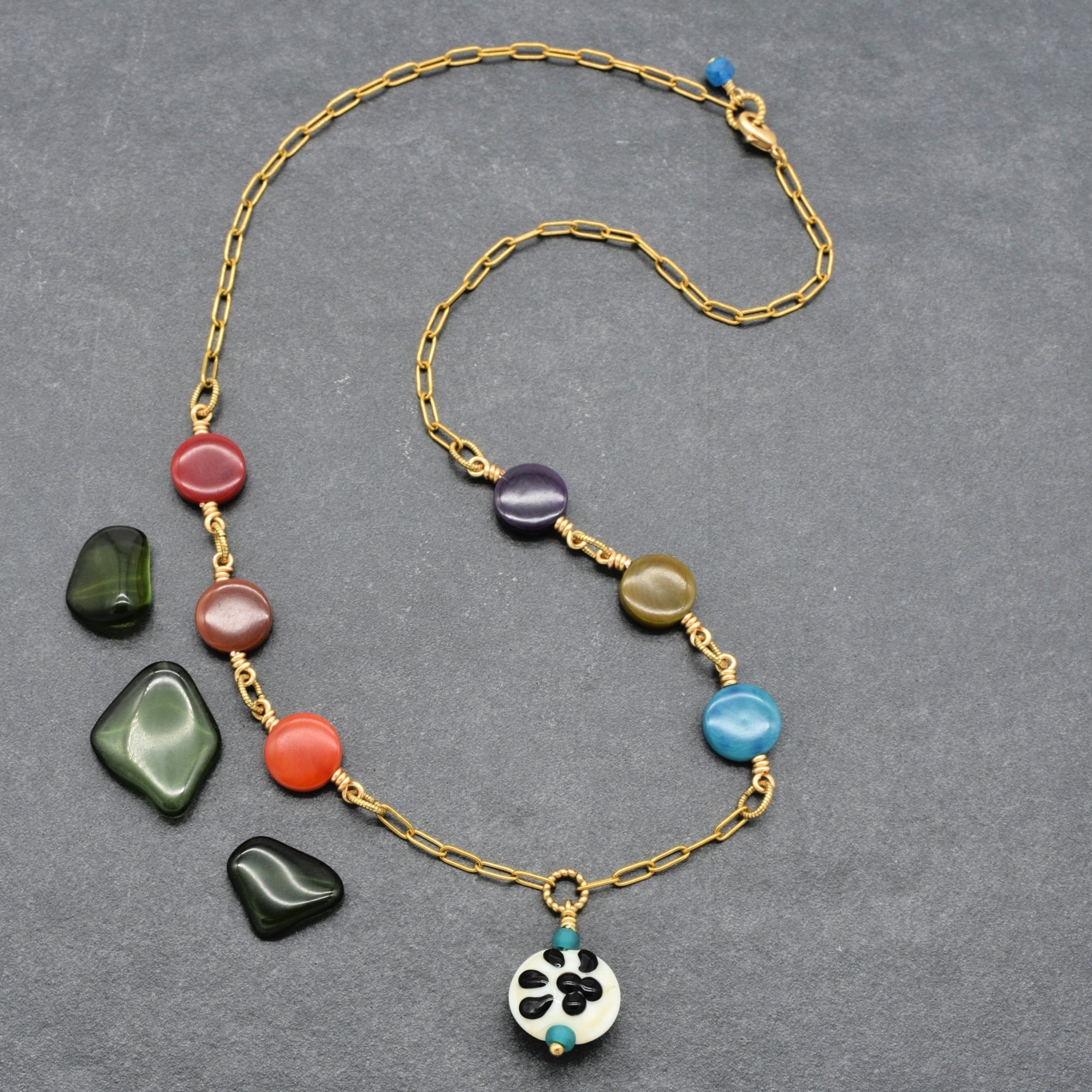 A gold chain necklace with colorful tagua nut coin beads and a white paw print pendant, displayed on a textured gray background - made with love in Colorado by Ruby Acorn.