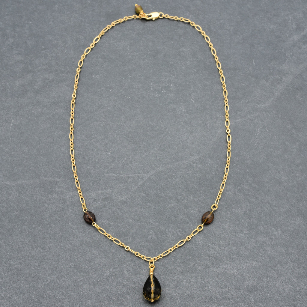 This image shows a necklace. The jewelry has a gold chain with a clasp and features small beads and a teardrop-shaped pendant hanging in the center. The length and design suggest that it is worn around the neck, making it a necklace rather than an earring or a bracelet.