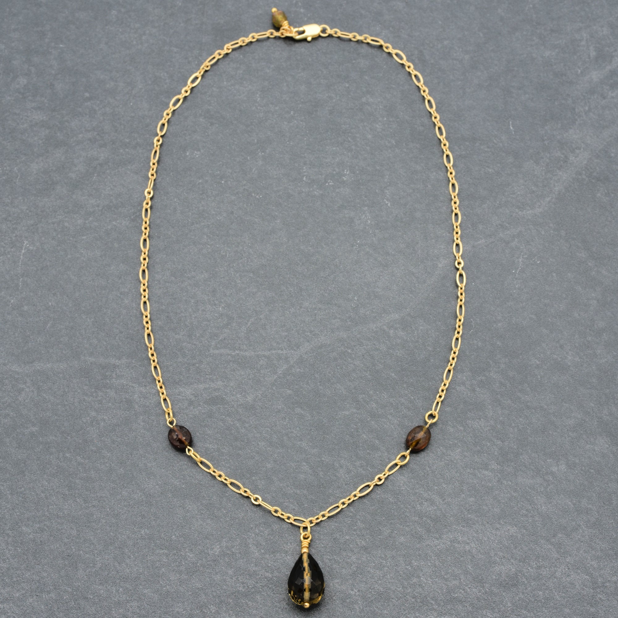 This image shows a necklace. The jewelry has a gold chain with a clasp and features small beads and a teardrop-shaped pendant hanging in the center. The length and design suggest that it is worn around the neck, making it a necklace rather than an earring or a bracelet.