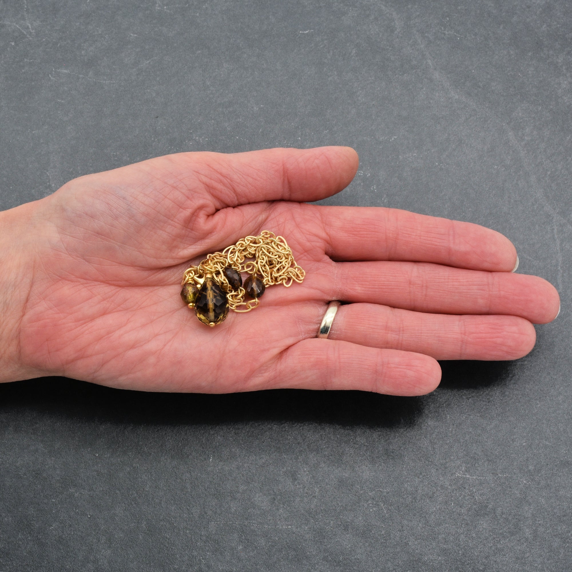 This image shows a hand holding a piece of jewelry with a gold chain and some dark-colored gemstones. Based on the length and design of the chain and the fact that it is being held loosely in the hand rather than as a pair or in a circular form fitting the wrist, it is most likely a necklace.