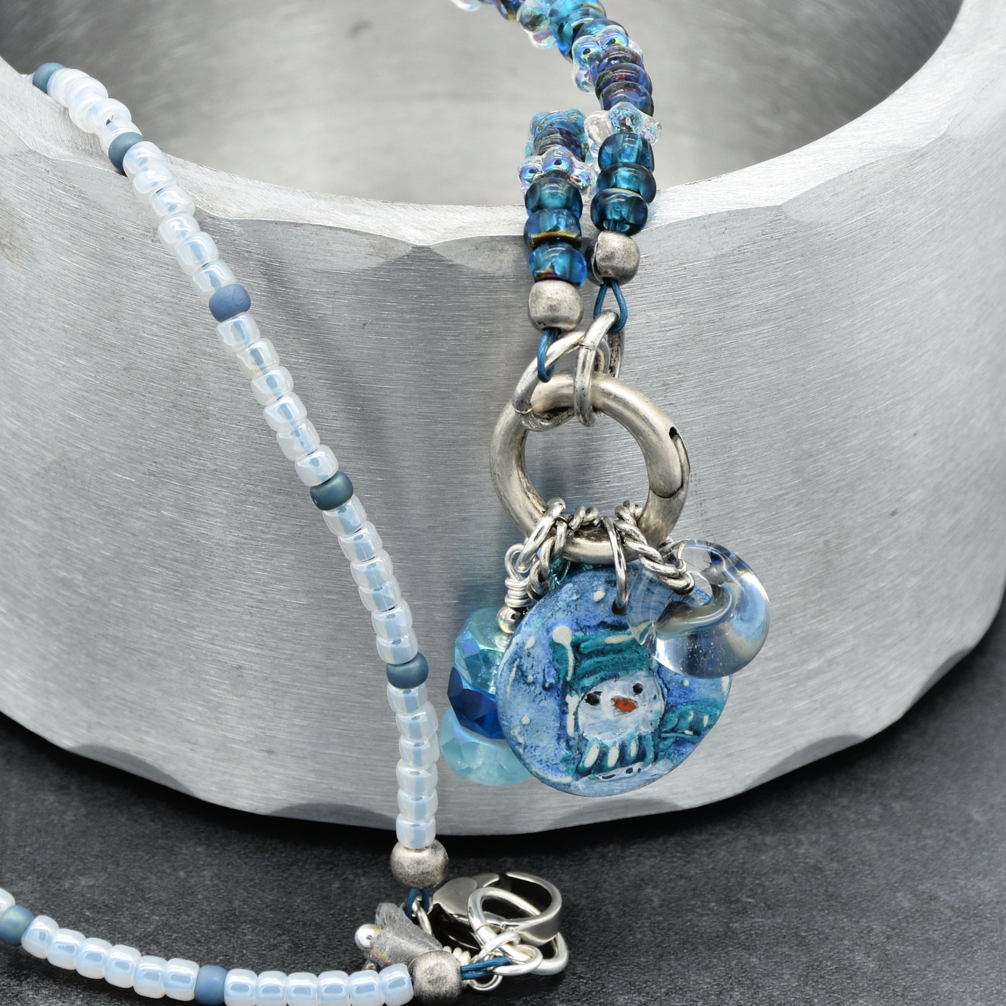 Beaded necklace with blue and silver charms on a stone surface