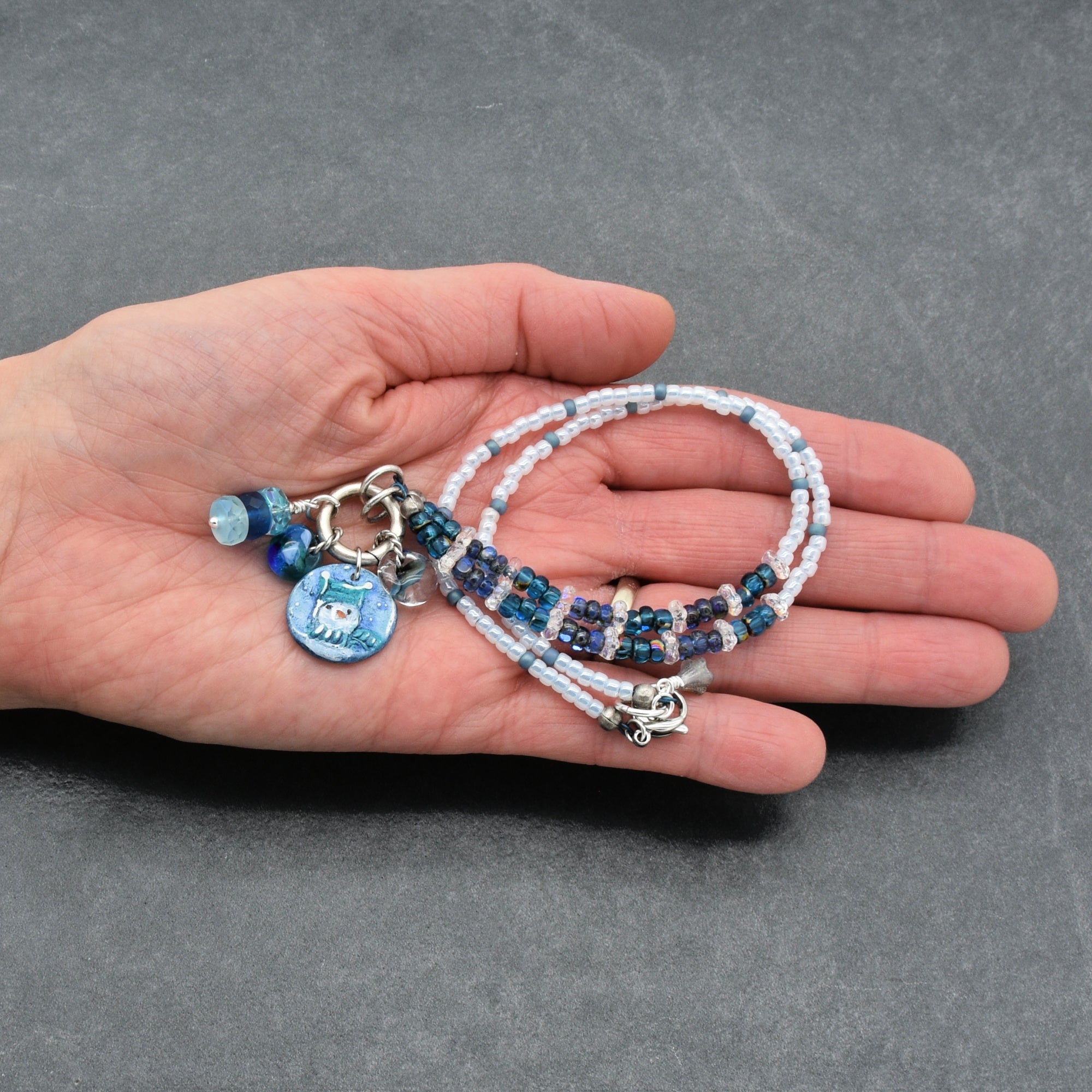 Hand holding festive beaded necklace with charms on a gray background