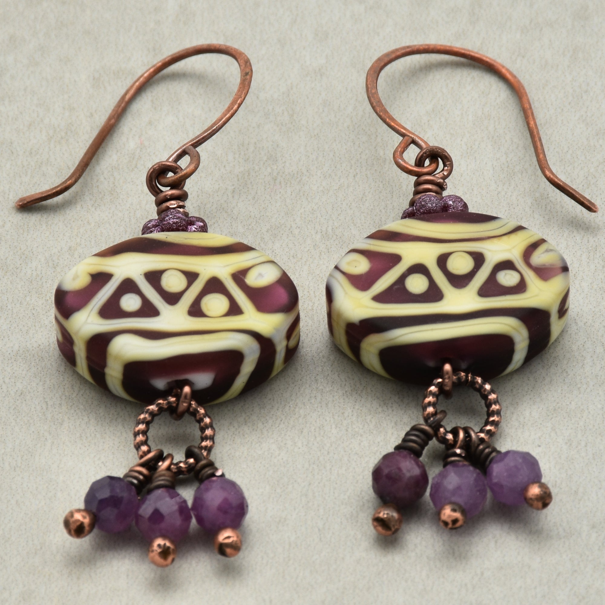 Pair of earrings with purple beads and patterned stones on a light gray background