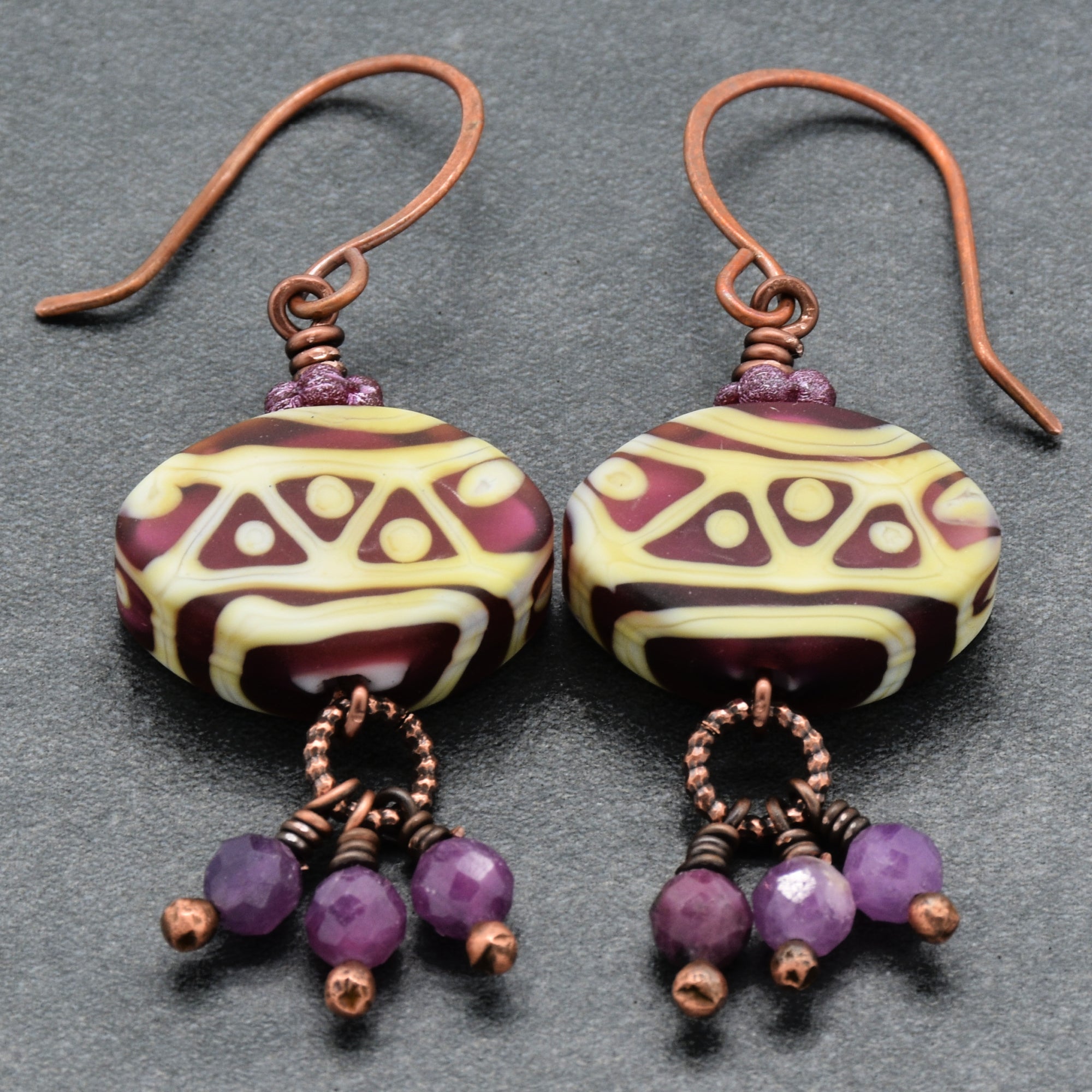 Pair of earrings with patterned beads and purple accents on a gray background