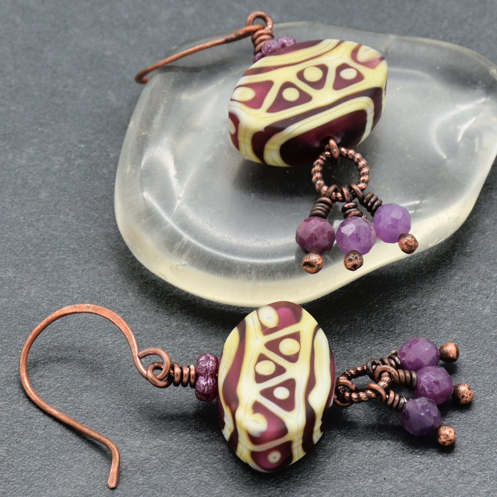 Pair of earrings with purple beads and patterned beads on a gray surface