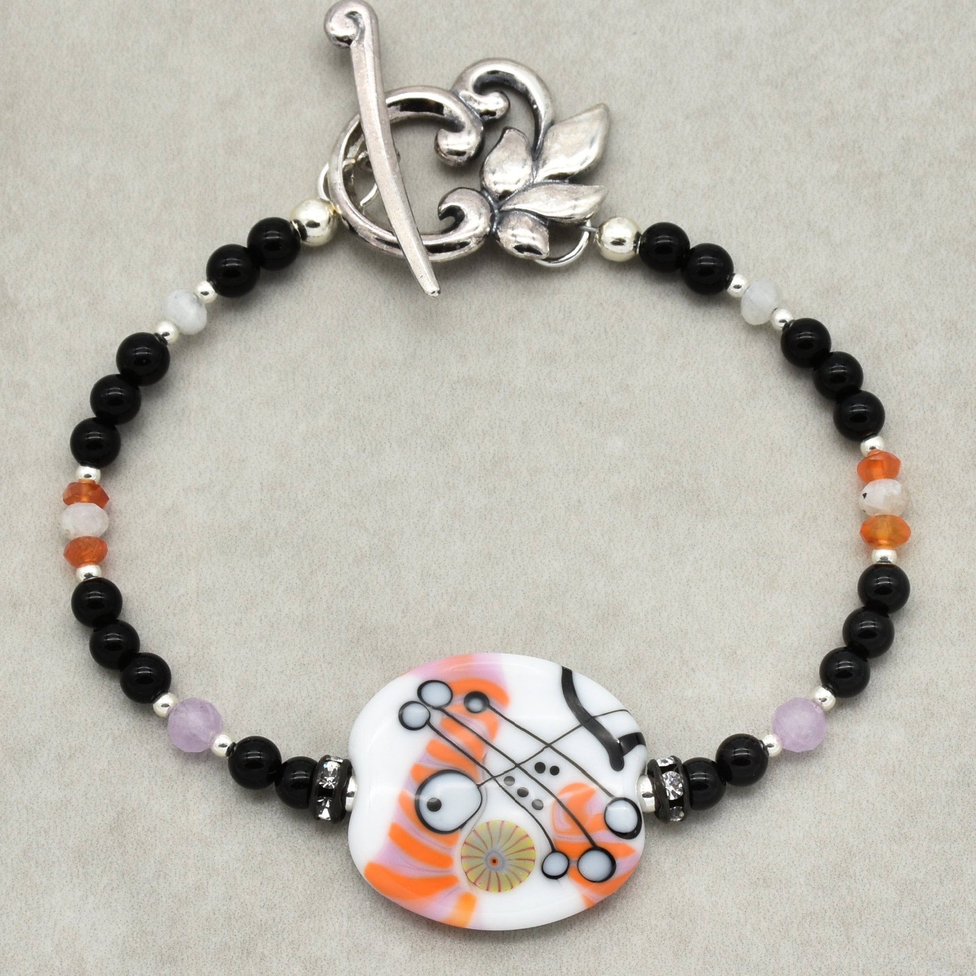 Bracelet with black, orange, and white beads on a gray background