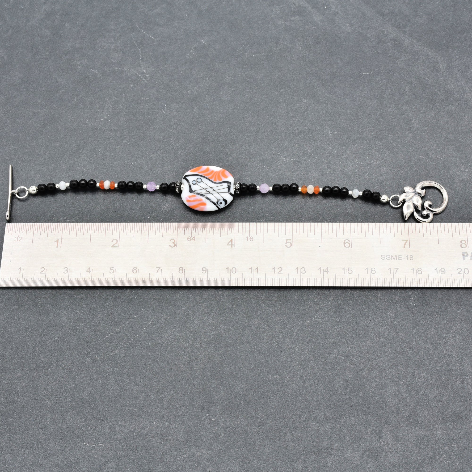 Beaded bracelet with a decorative clasp on a gray surface, measured against a ruler.