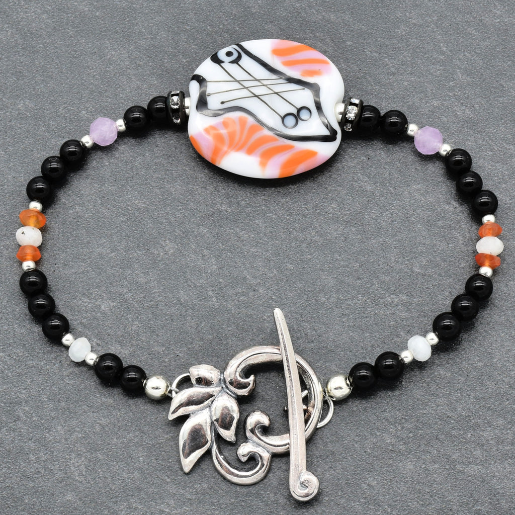 Bracelet with black beads, silver clasp, and colorful pendant on a gray background