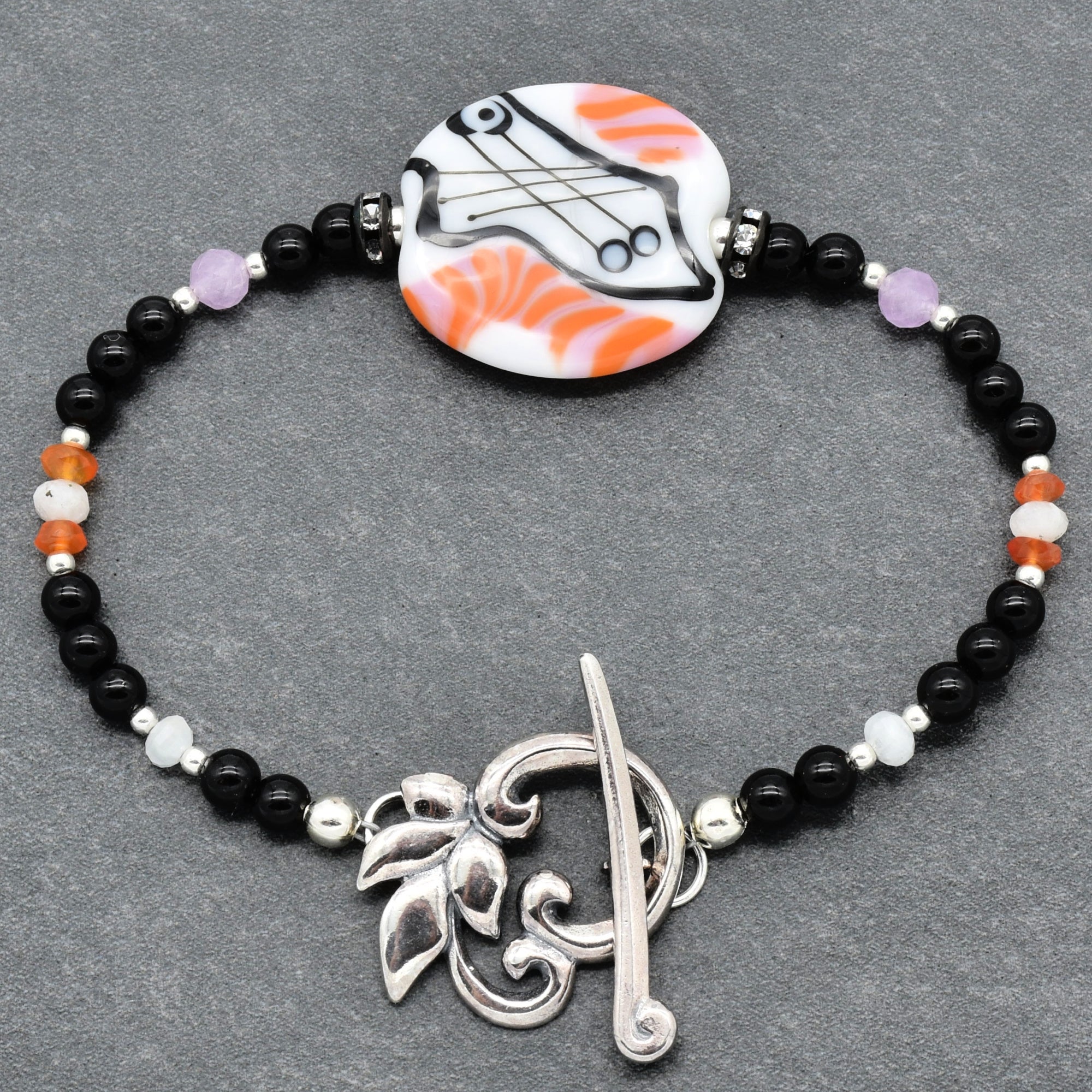 Bracelet with black beads, silver clasp, and colorful pendant on a gray background
