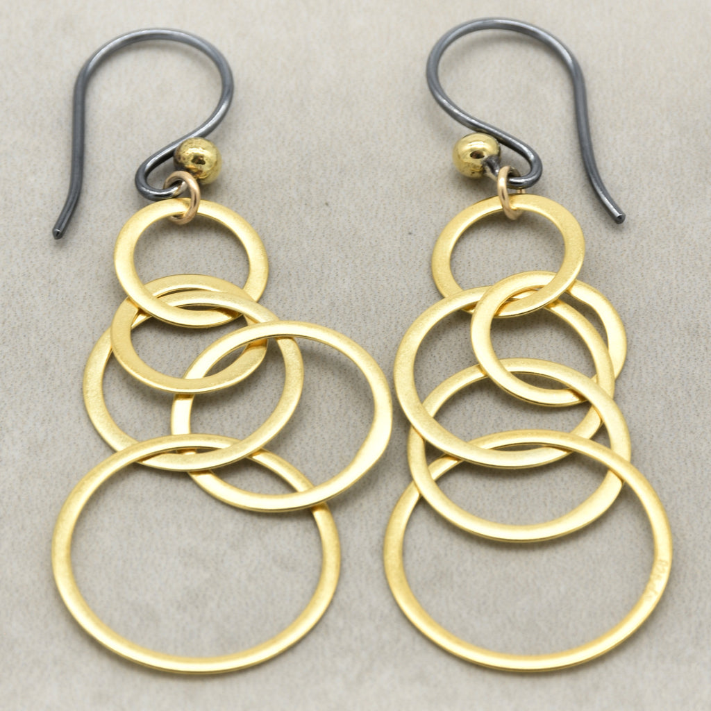 A pair of gold and silver drop earrings featuring multiple interlocking circular rings, photographed on a neutral textured gray background - made with love by Ruby Acorn.