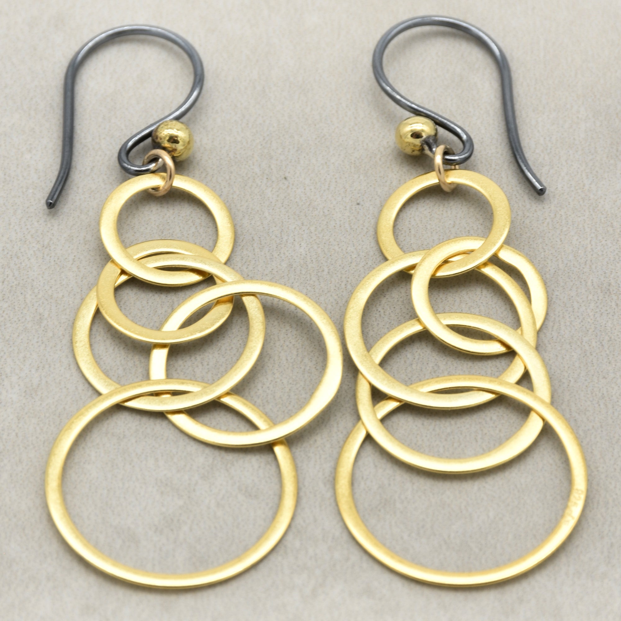 A pair of gold and silver drop earrings featuring multiple interlocking circular rings, photographed on a neutral textured gray background - made with love by Ruby Acorn.