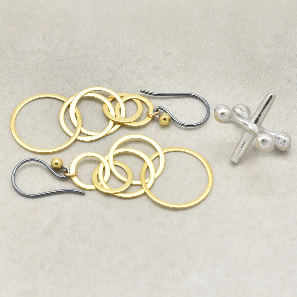 A pair of gold and silver dangle earrings with interlocking circular rings, small gold beads, and black silver ear wires, displayed on a beige background - made with love by Ruby Acorn.