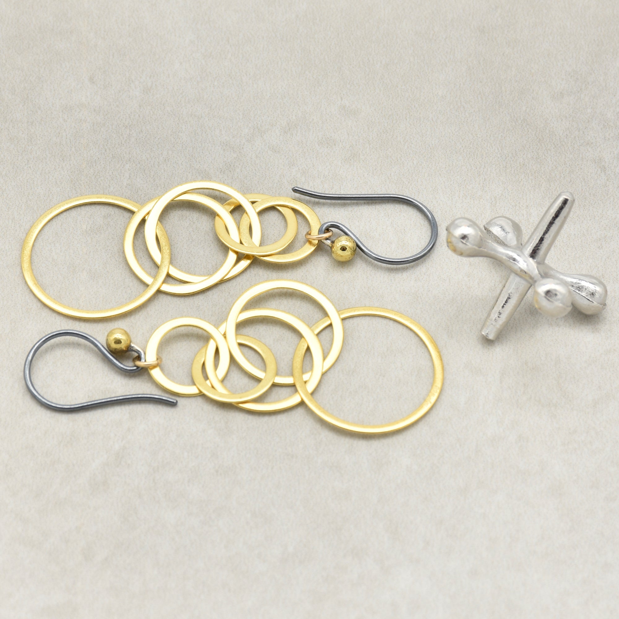 A pair of gold and silver dangle earrings with interlocking circular rings, small gold beads, and black silver ear wires, displayed on a beige background - made with love by Ruby Acorn.