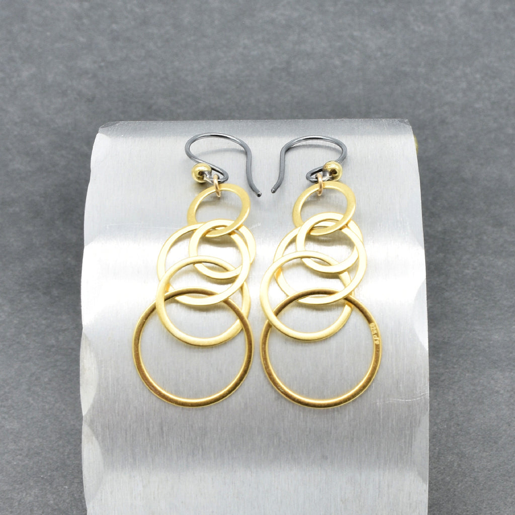 Gold interlocking hoop earrings with black silver ear wires on a silver circular display - made with love by Ruby Acorn.