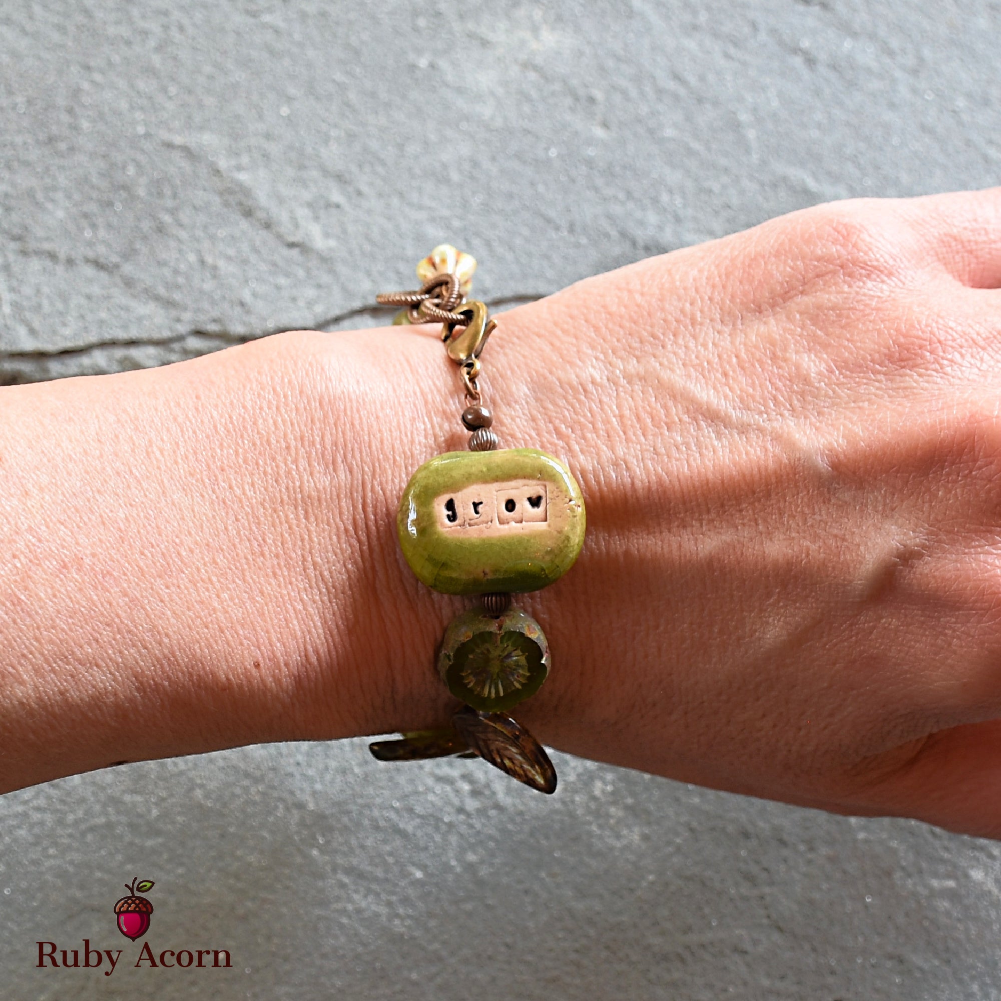 The image shows a bracelet. It is worn around the wrist and features a green bead with the word "grow" inscribed on it.