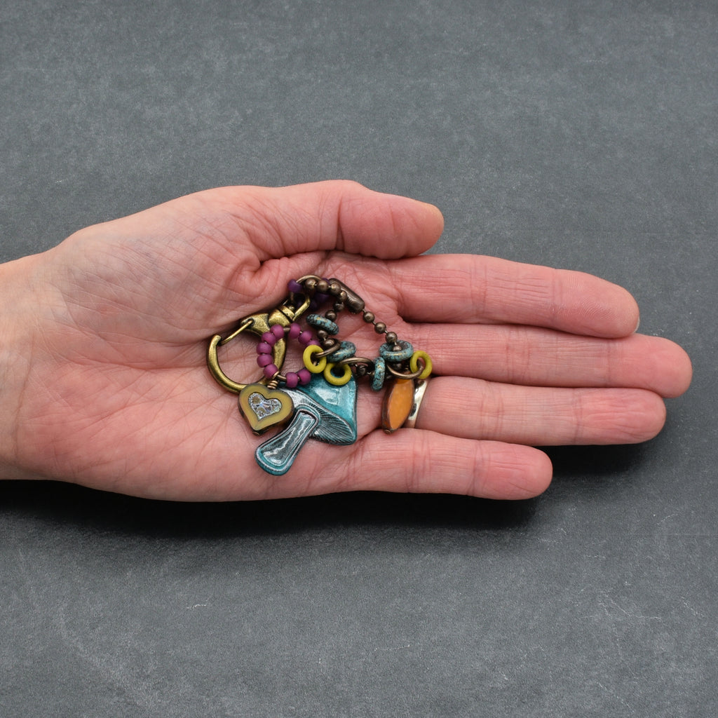 Hand holding a colorful keychain with various charms against a gray background