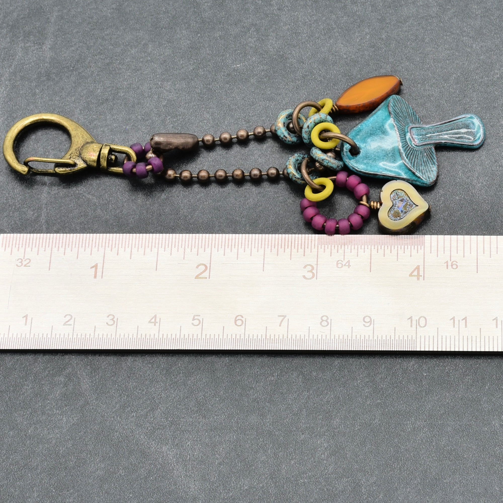 Colorful keychain with charms on a gray surface with a ruler for scale.