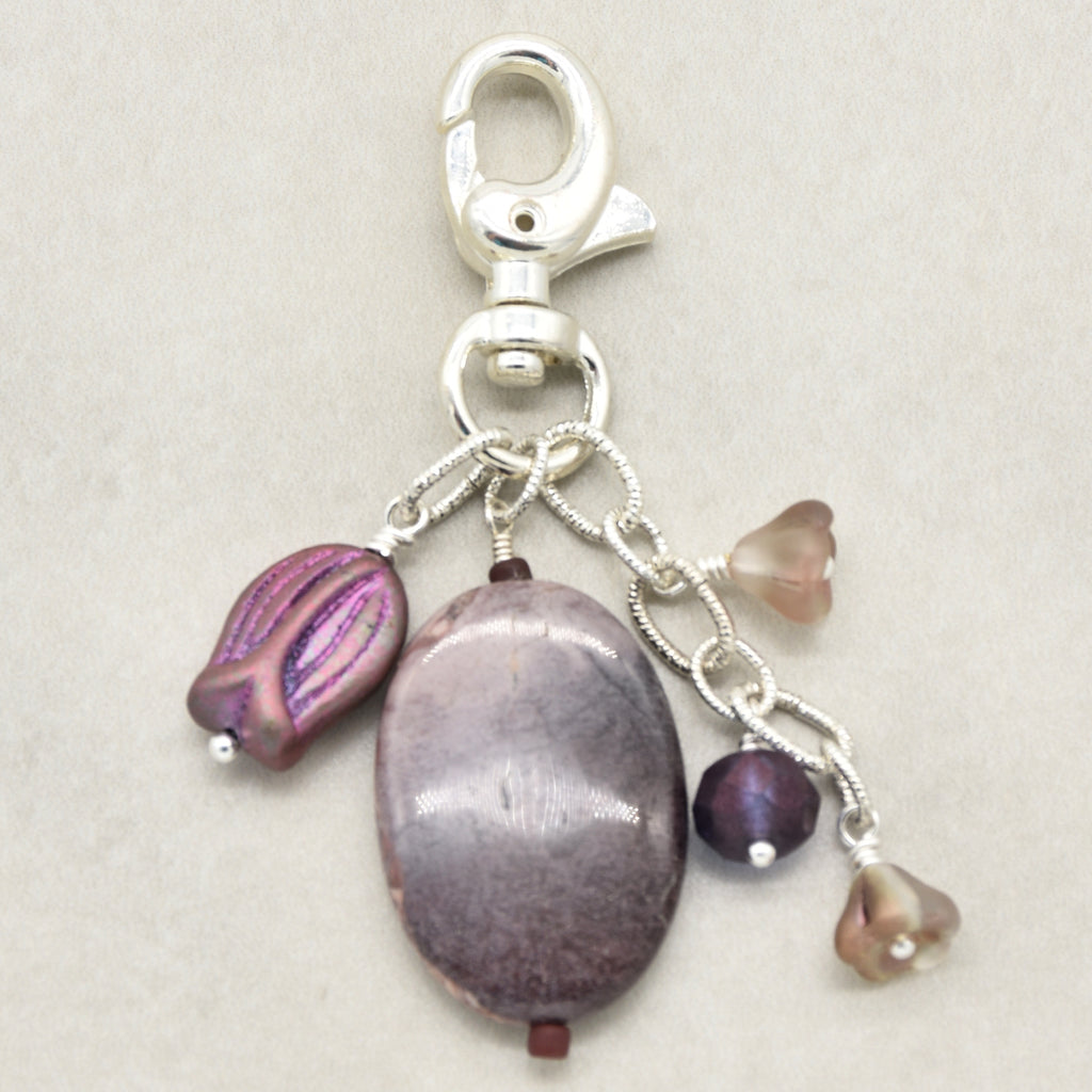 A silver lobster clasp keychain charm featuring a porcelain jasper focal, a purple iridescent bead, and three smaller floral beads in mauve and brown, set against a neutral beige background - made with love in Colorado by Ruby Acorn.