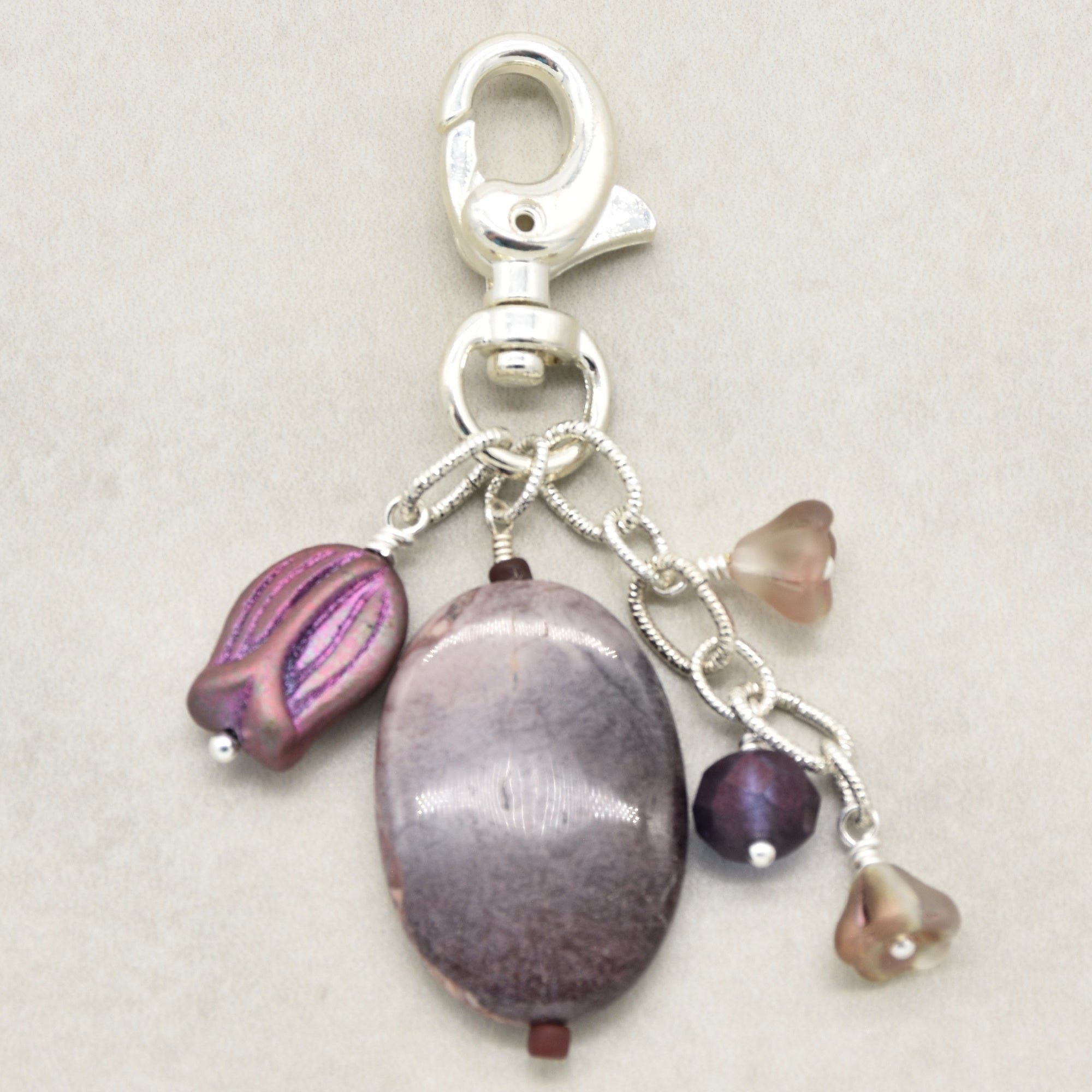 A silver lobster clasp keychain charm featuring a porcelain jasper focal, a purple iridescent bead, and three smaller floral beads in mauve and brown, set against a neutral beige background - made with love in Colorado by Ruby Acorn.