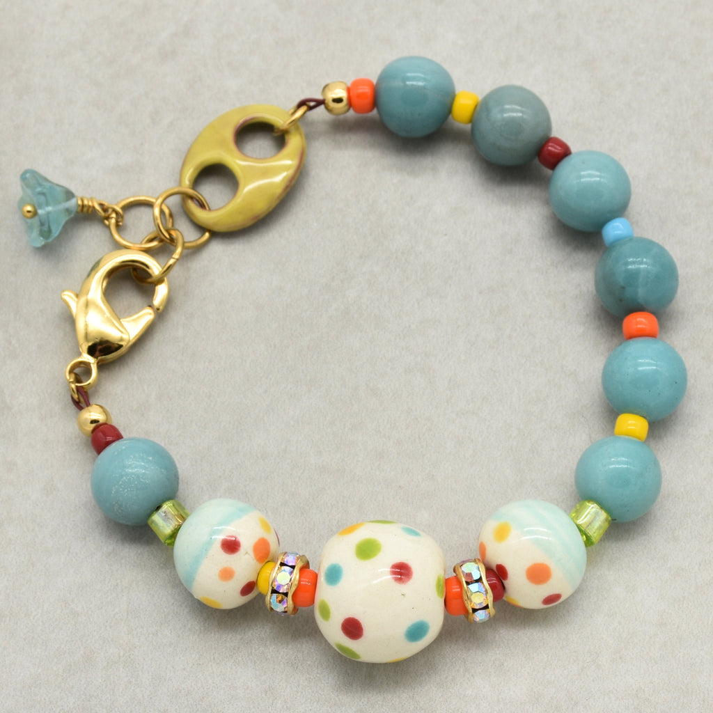 A handmade beaded bracelet featuring light blue amazonite beads, white ceramic beads with colorful polka dots, and small accent beads in orange, yellow, and red, finished with a gold-toned lobster clasp.