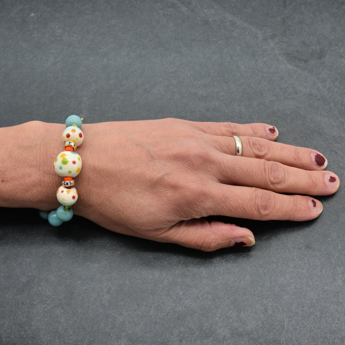 A close-up of a person's hand wearing a beaded bracelet. The bracelet features light blue beads, white beads with colorful polka dots, and small orange spacer beads.
