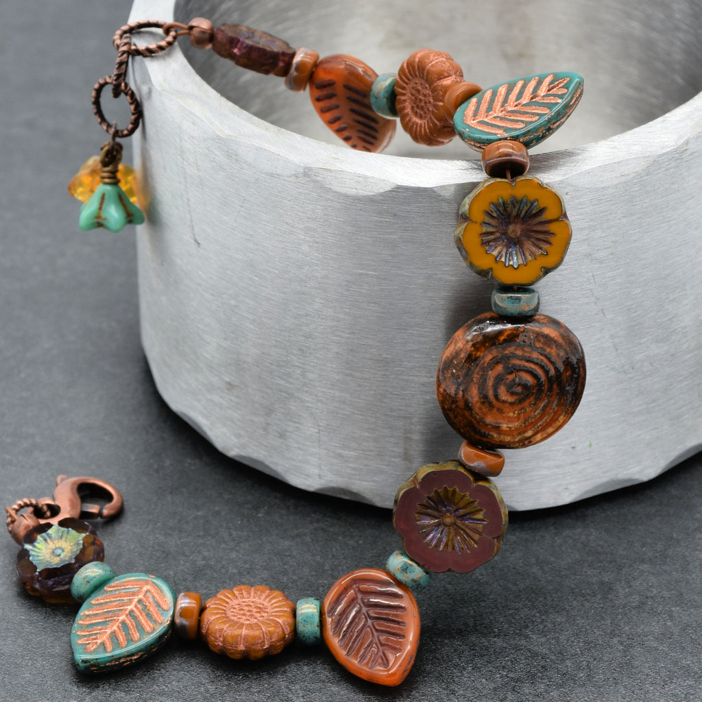 Colorful beaded bracelet with floral and leaf designs on a gray surface.