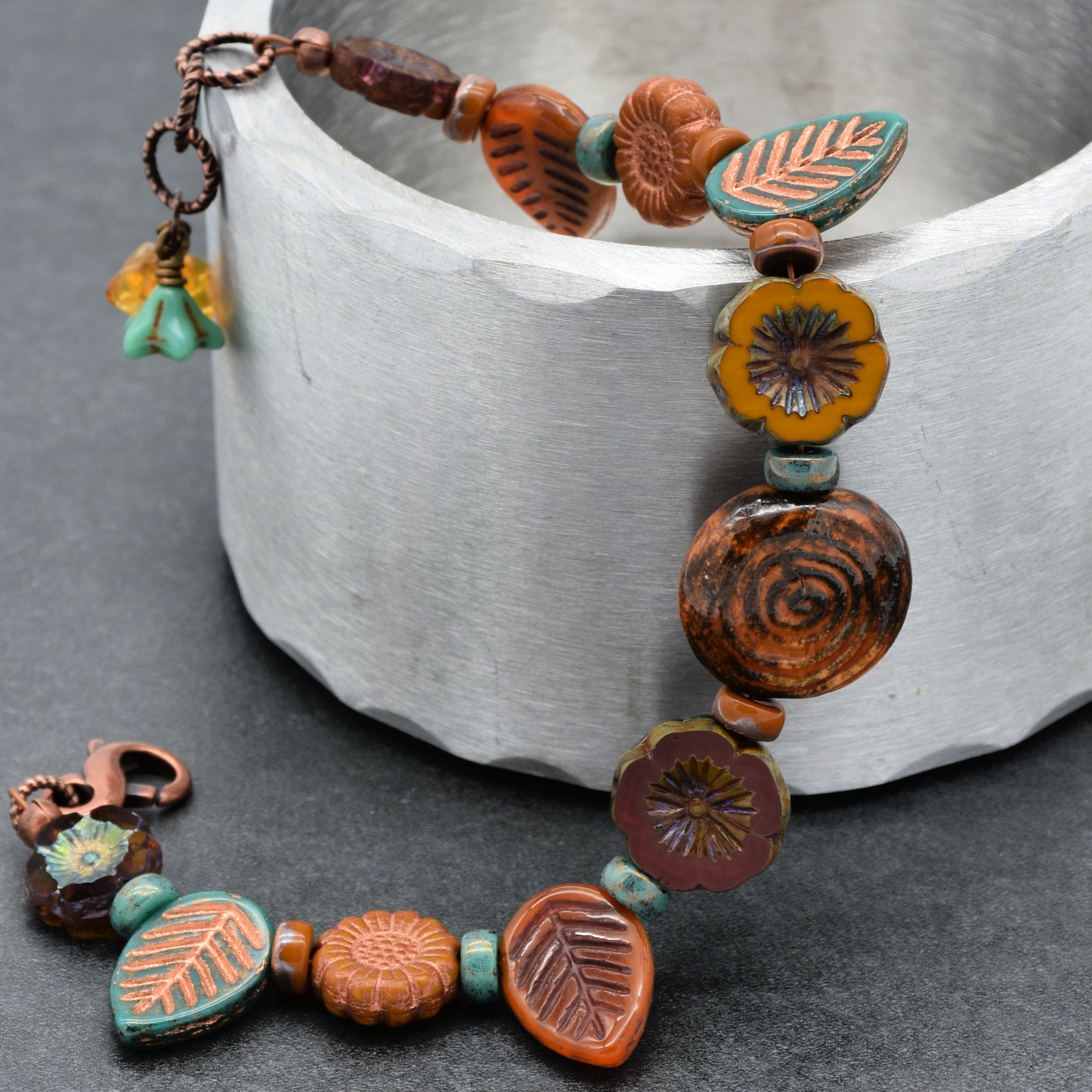 Colorful beaded bracelet with floral and leaf designs on a gray surface.