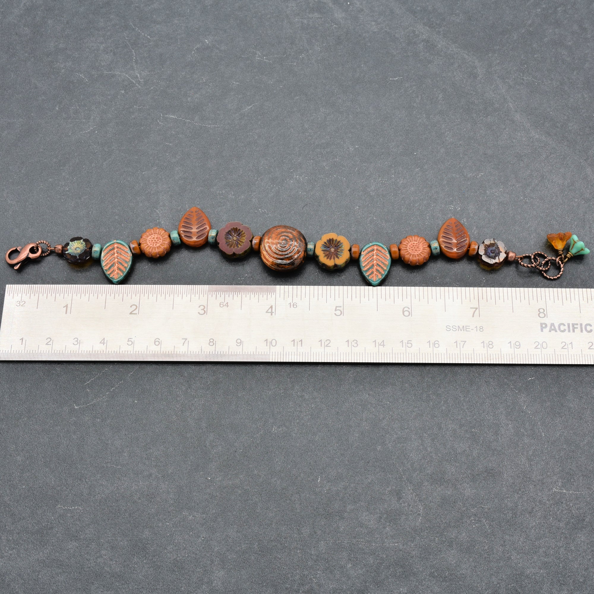Bracelet with decorative beads on a gray surface with a ruler for scale.