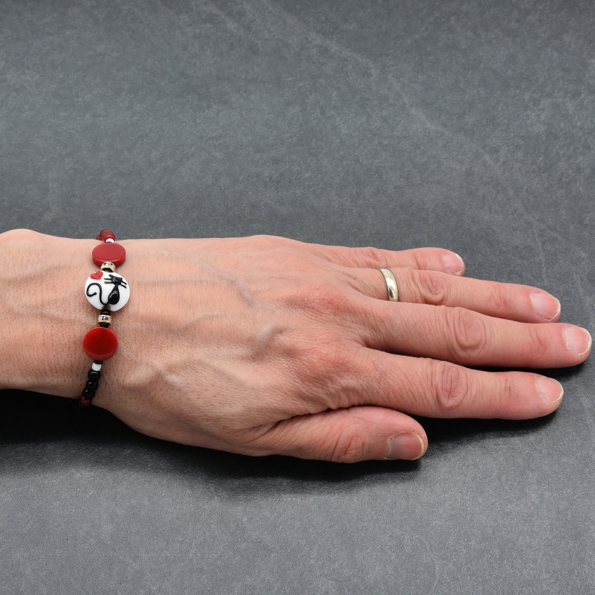Hand wearing a bracelet with a cat focal and black and red beads on a gray background