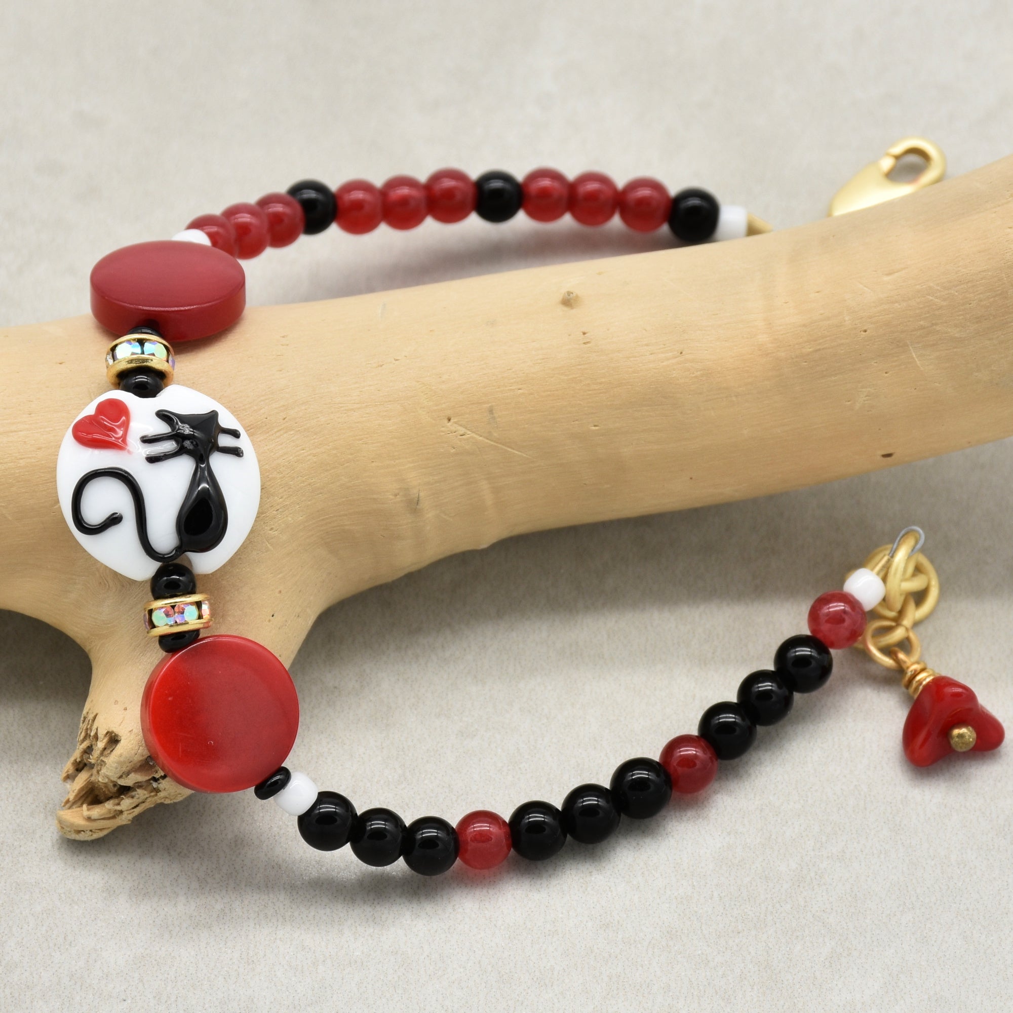 Beaded bracelet with a cat focal and  red, black, and white beads on a wooden branch