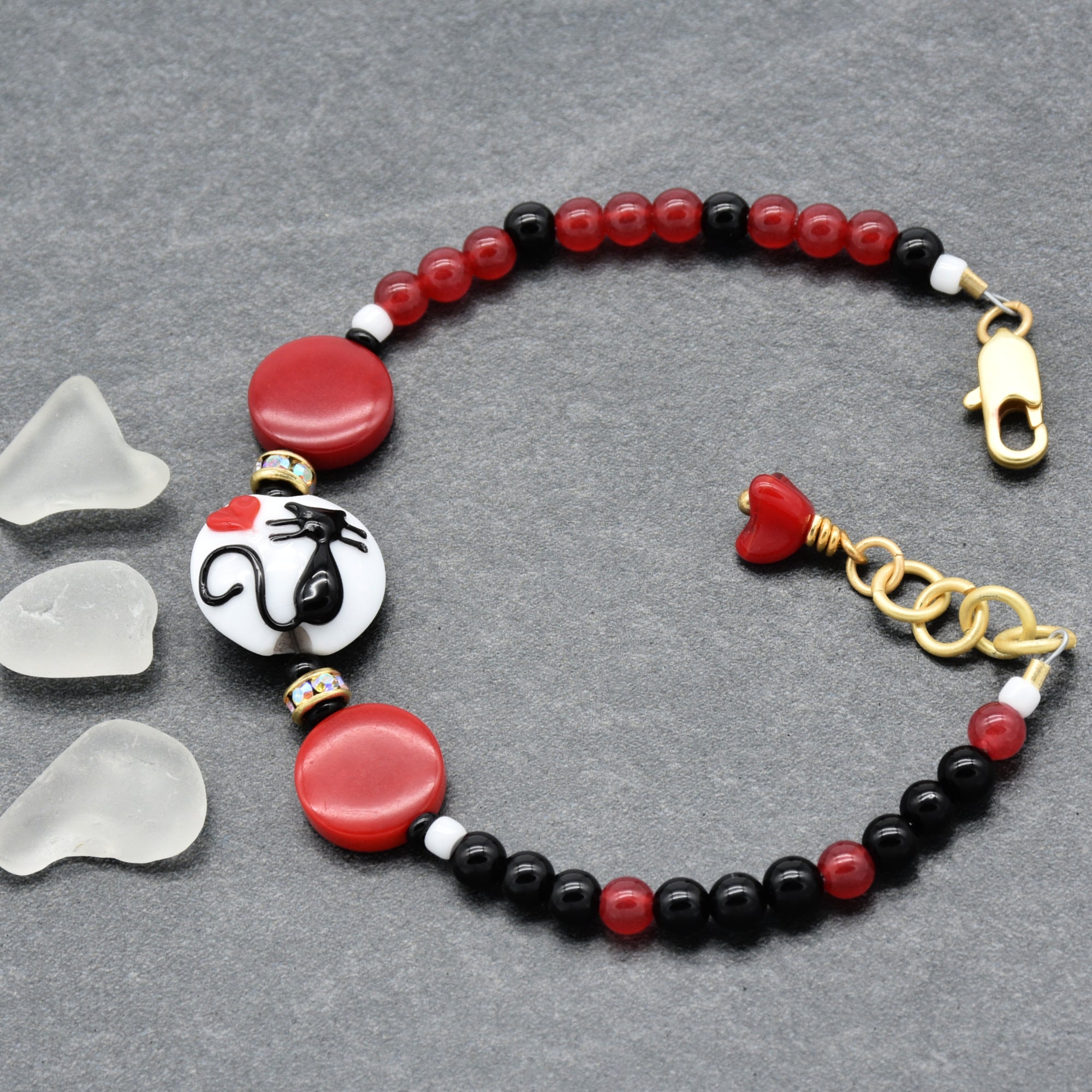 Beaded bracelet with cat focal,  red, black, and gold elements on a gray background