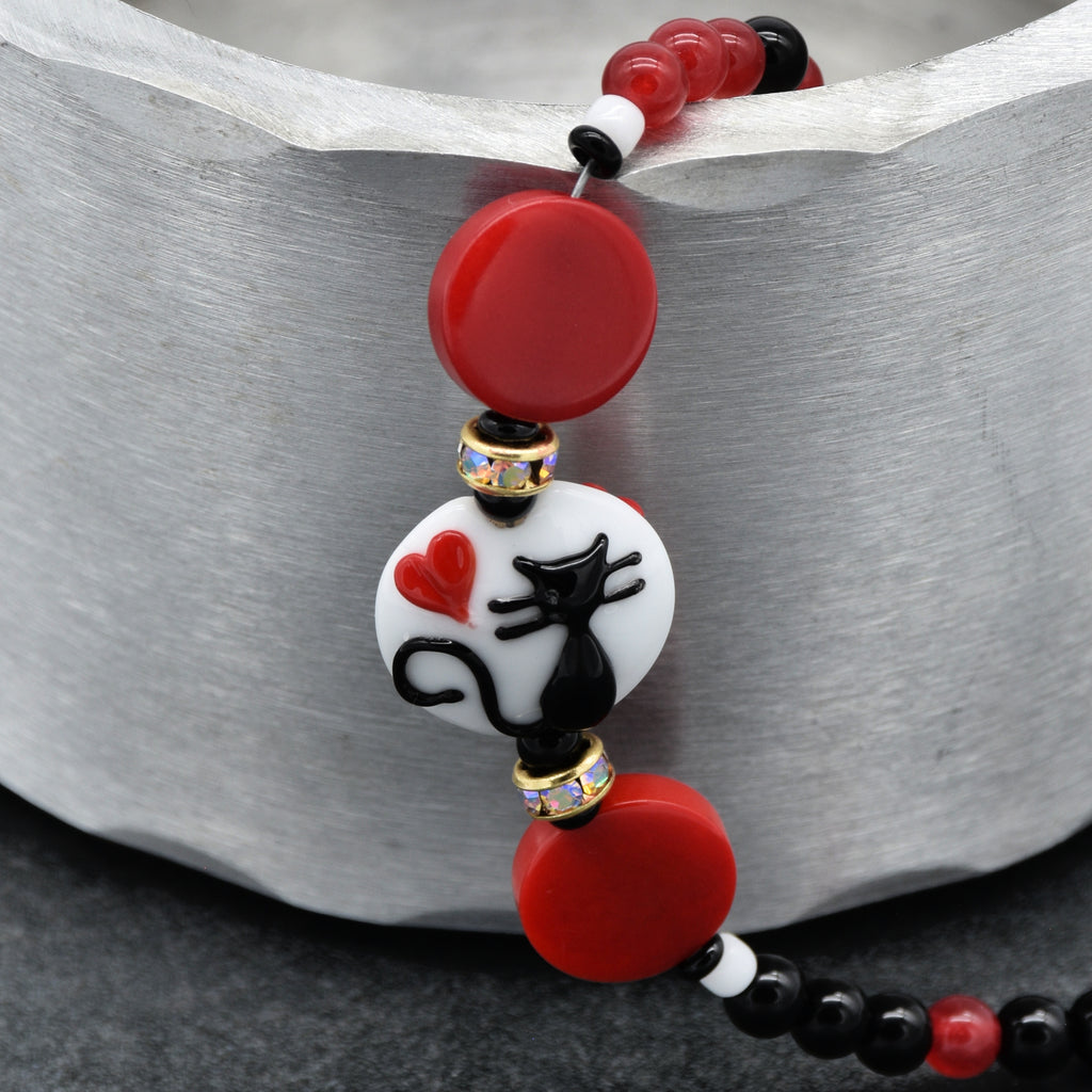 Beaded bracelet with a black cat and red, black and white beads on a metallic surface