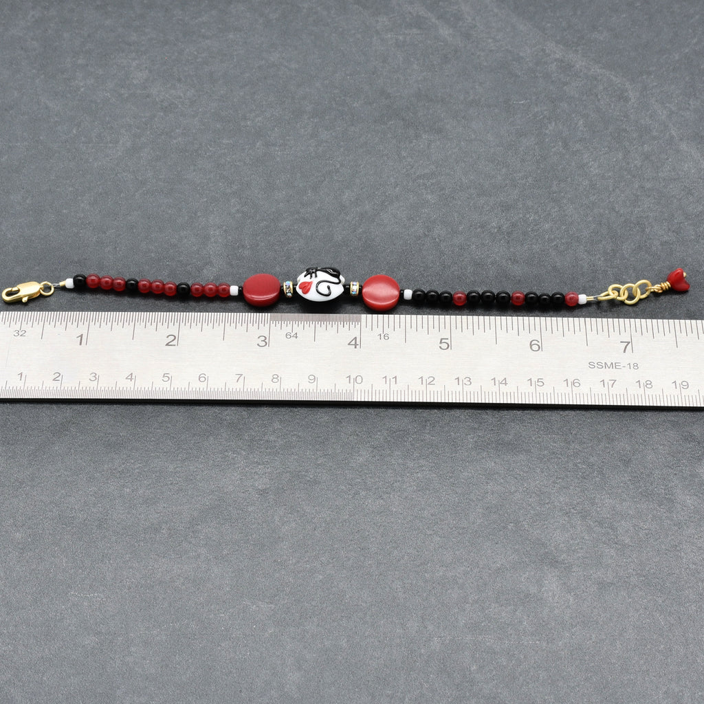 Beaded bracelet with red, black, and gold accents on a gray surface with a ruler for scale.