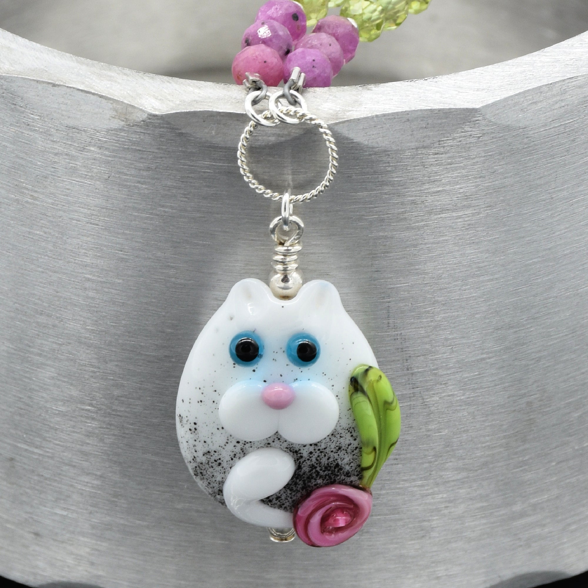 Cat-shaped pendant with pink flower on a silver chain against a gray background