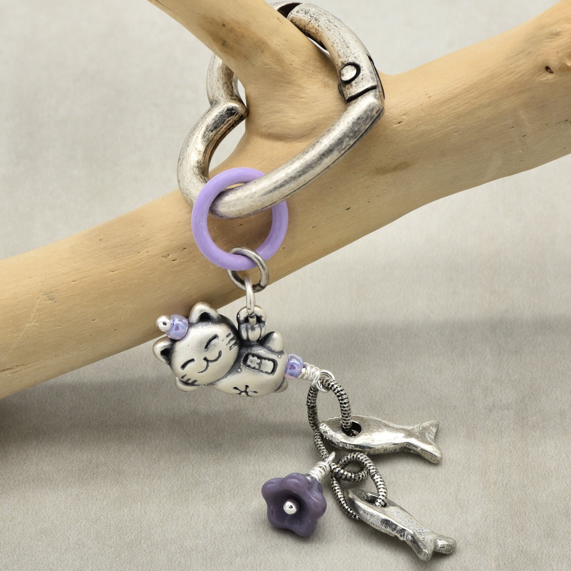 Silver charm keychain with cat and flower charms on a wooden branch
