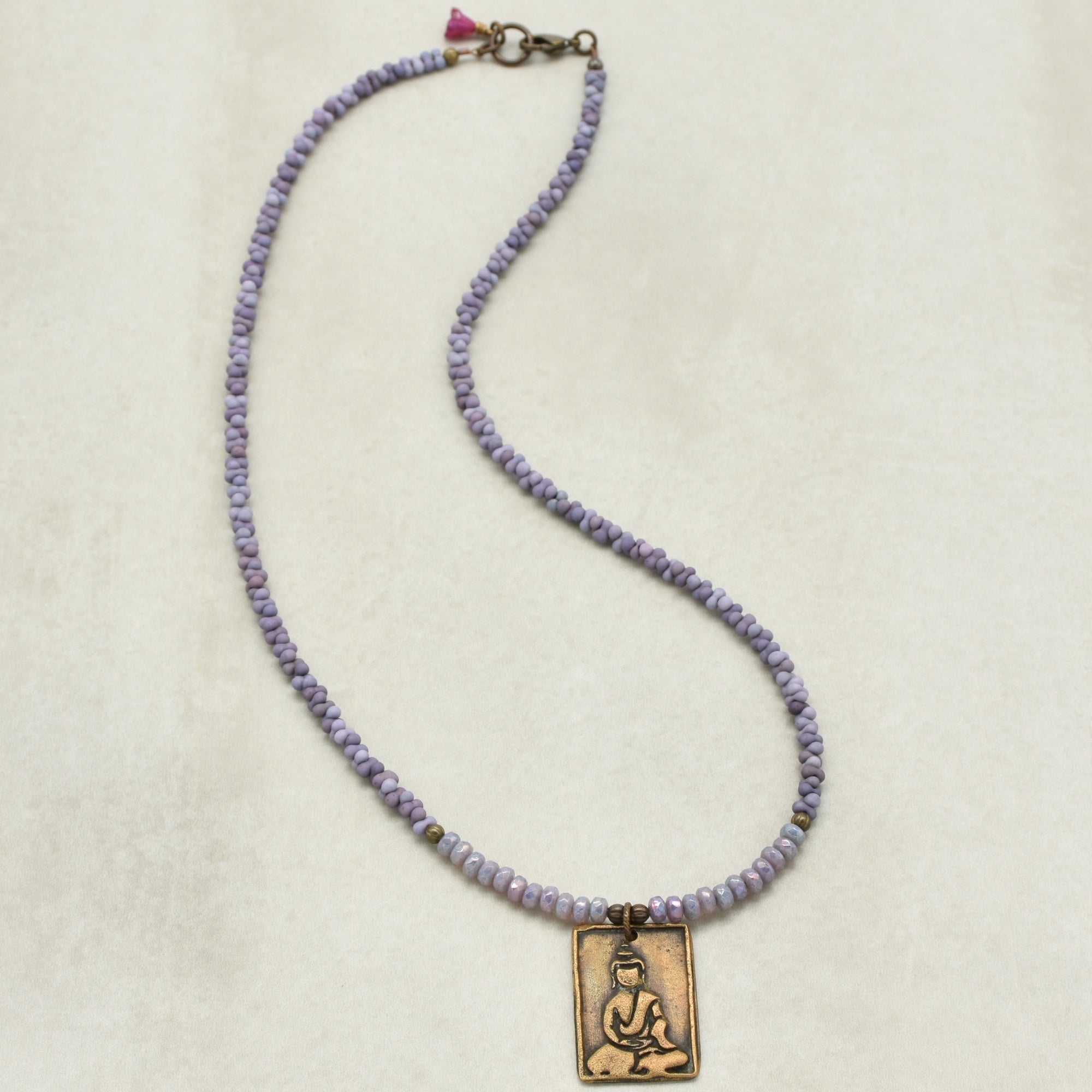 Necklace with purple beads and a Buddha pendant on a beige background
