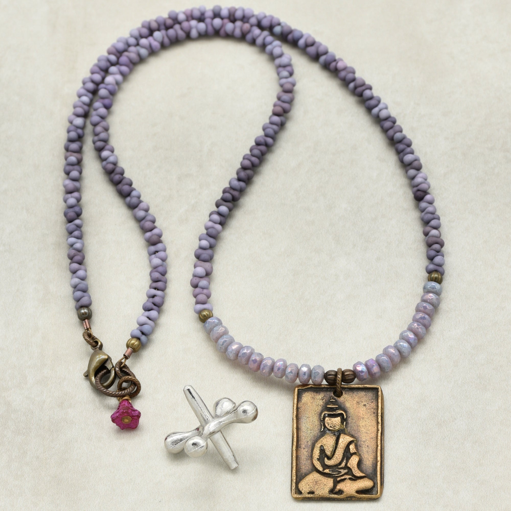 Necklace with purple beads and a Buddha pendant on a beige background