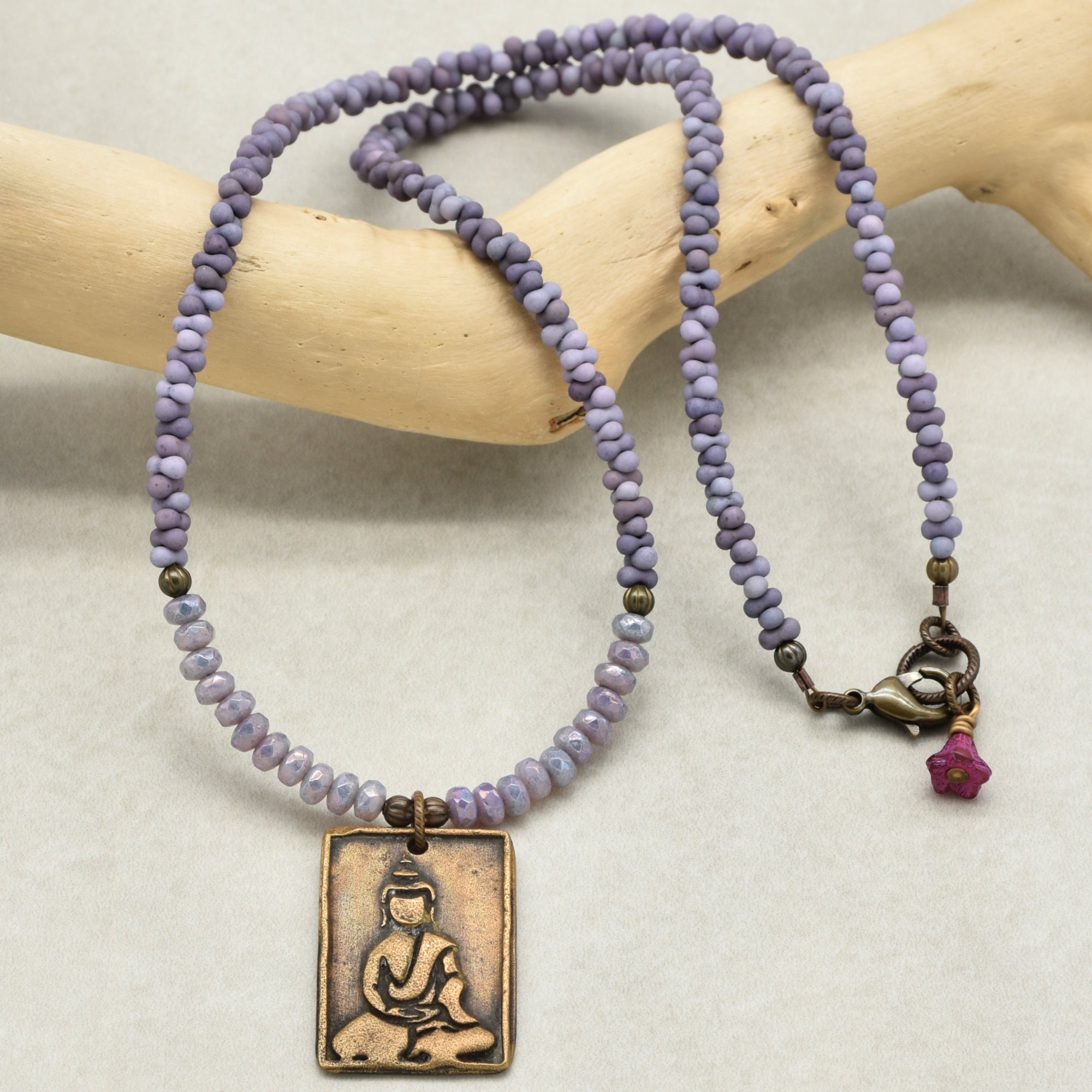 Necklace with purple beads and a Buddha pendant on a wooden branch.