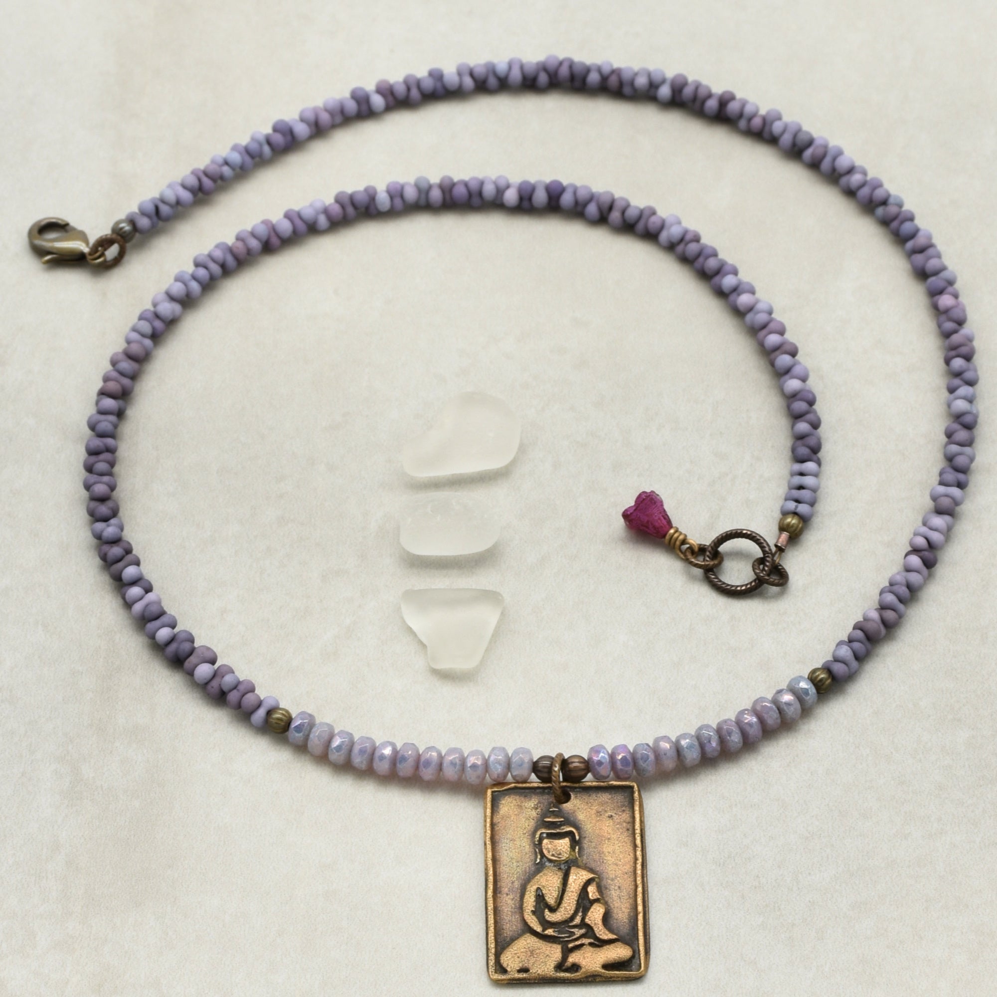 Purple beaded necklace with a bronze pendant featuring a Buddha on a white background