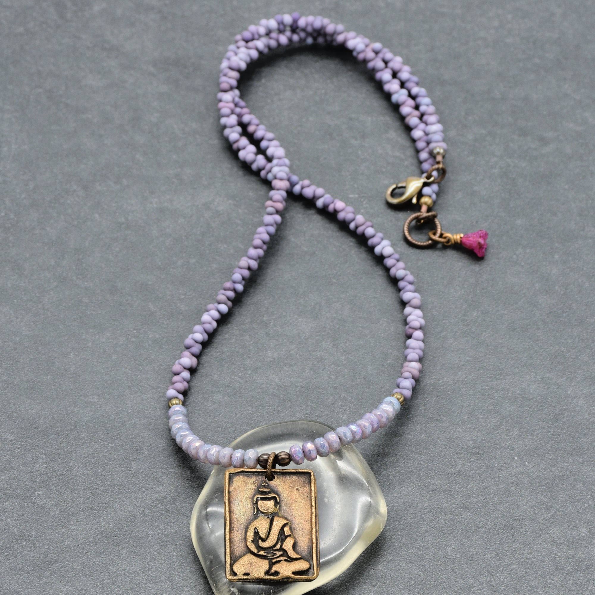 Purple beaded necklace with a Buddha pendant on a gray background