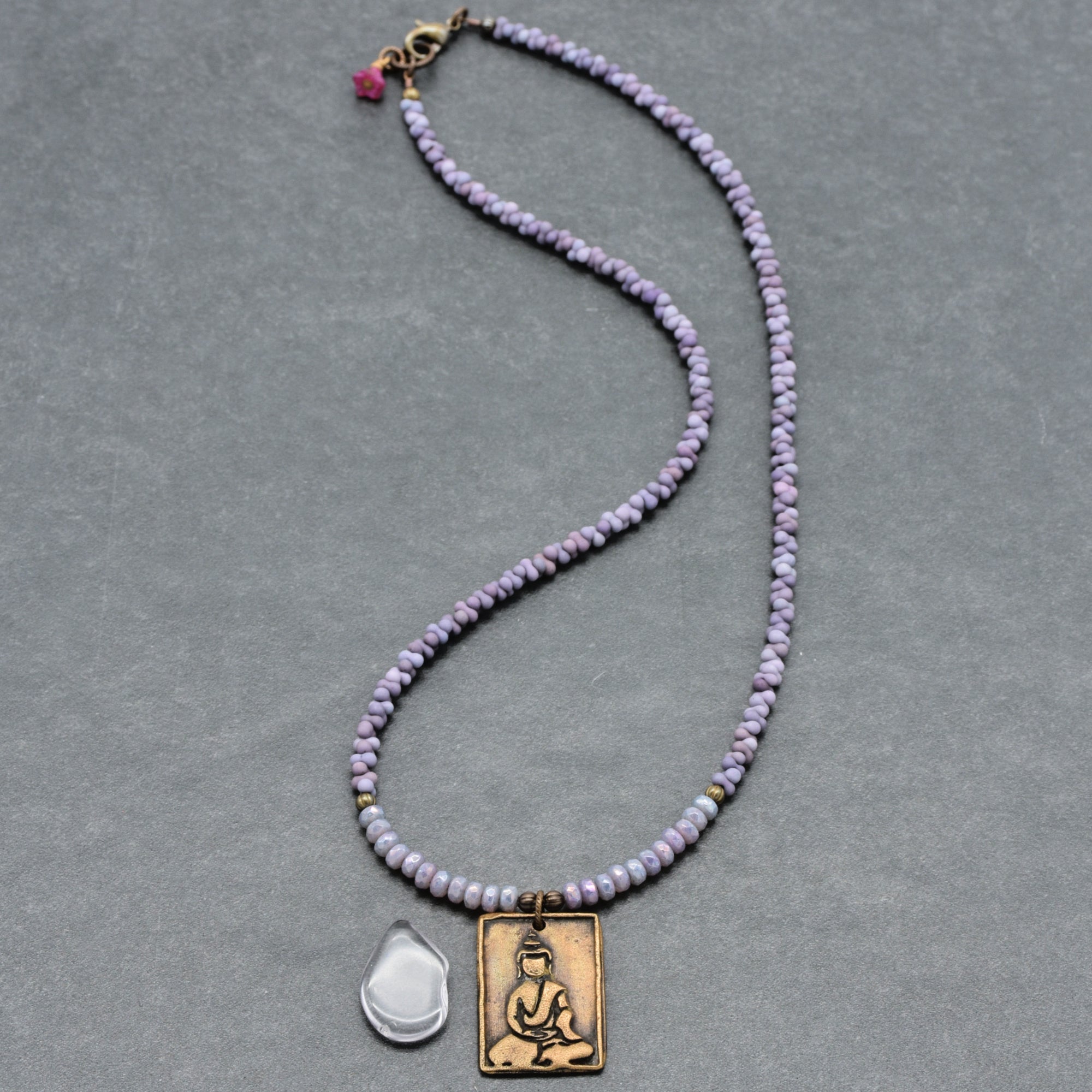 Necklace with purple beads and a brass Buddha pendant on a gray background