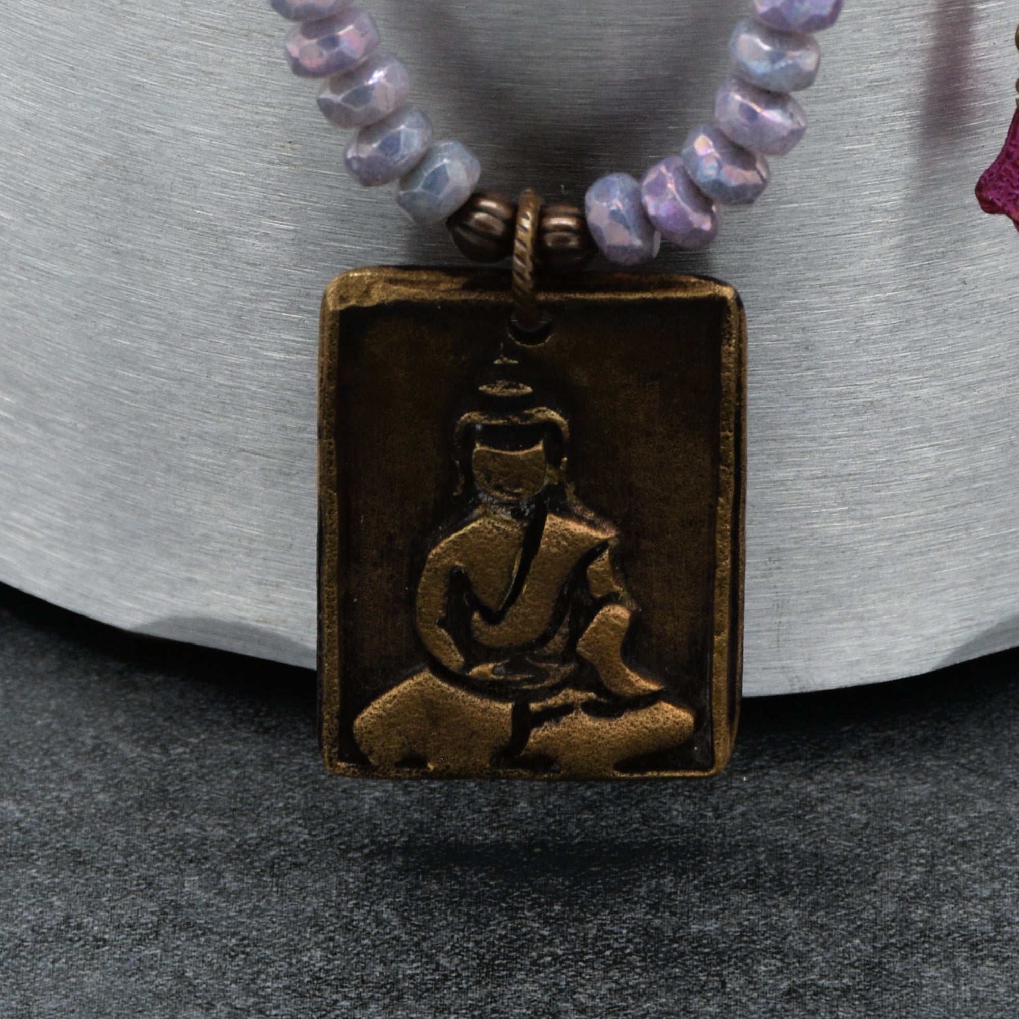 Necklace with a bronze pendant featuring a Buddha on a textured surface