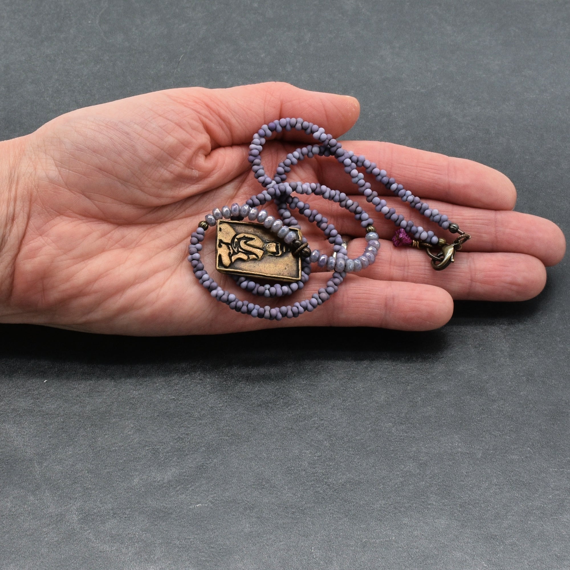 Hand holding a necklace with a Buddha  pendant on a gray background