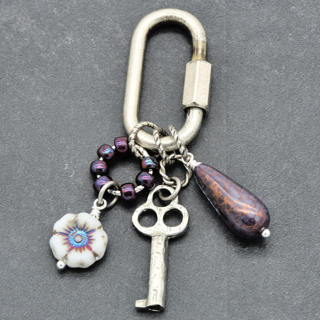 Keychain with various charms including a key, flower, and purple bead on a gray background